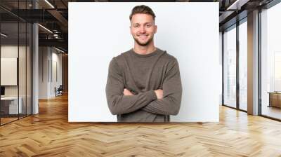 Young blonde caucasian man isolated on white background keeping the arms crossed in frontal position Wall mural