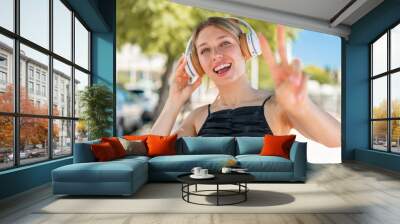 Young blonde woman at outdoors listening music and singing Wall mural