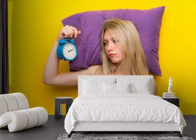 Young blonde woman in pajamas holding vintage clock Wall mural