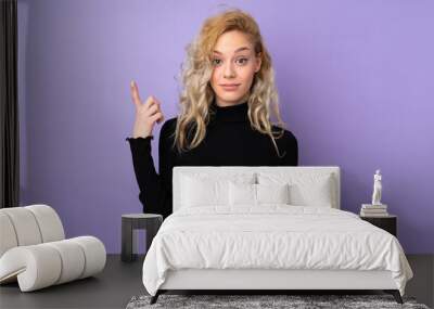 Young blonde woman isolated on purple background pointing with the index finger a great idea Wall mural