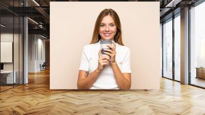 Young blonde woman over isolated background holding coffee to take away Wall mural