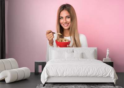 Young blonde woman over isolated pink background holding a bowl of cereals Wall mural