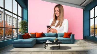 Young blonde woman over isolated pink background sending a message or email with the mobile Wall mural