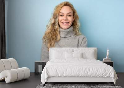 Young blonde woman wearing a sweater isolated on blue background keeping the arms crossed in frontal position Wall mural