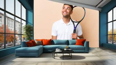 Young brazilian handsome man playing tennis isolated on beige background thinking an idea while looking up Wall mural