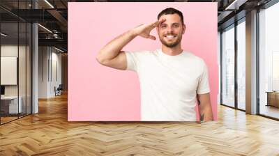 Young Brazilian man isolated on pink background saluting with hand with happy expression Wall mural