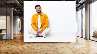 Young Brazilian man sitting on the floor isolated on white background laughing Wall mural