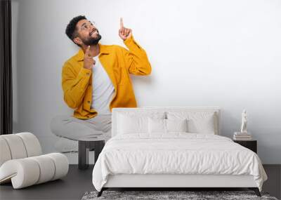 Young Brazilian man sitting on the floor isolated on white background pointing with the index finger a great idea Wall mural