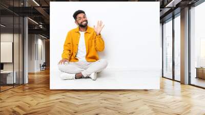 Young Brazilian man sitting on the floor isolated on white background saluting with hand with happy expression Wall mural