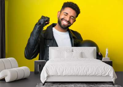 Young Brazilian man with a motorcycle helmet isolated on yellow background celebrating a victory Wall mural