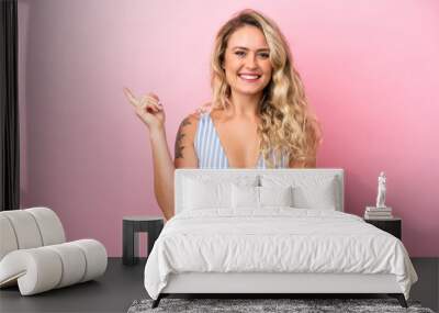 Young Brazilian woman in swimsuit in summer holidays isolated on pink background pointing finger to the side Wall mural