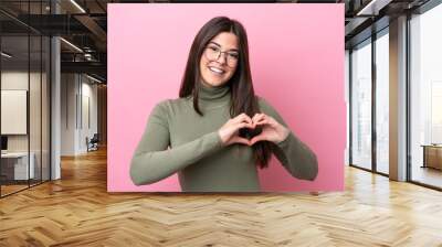 Young Brazilian woman isolated on pink background With glasses making heart with hands Wall mural