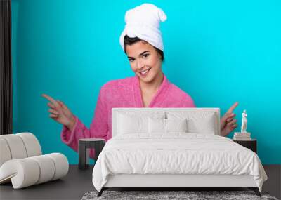 Young Brazilian woman with a bathrobe isolated on blue background pointing finger to the laterals and happy Wall mural