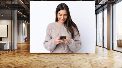 Young brunette woman over isolated white background sending a message with the mobile Wall mural