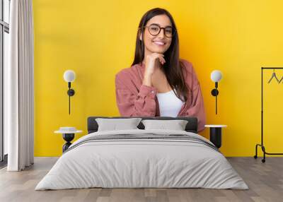 Young brunette woman over isolated yellow background with glasses and smiling Wall mural