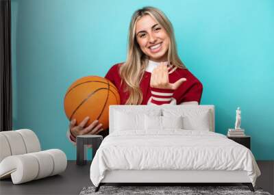 Young caucasian basketball player woman isolated on blue background inviting to come with hand. Happy that you came Wall mural