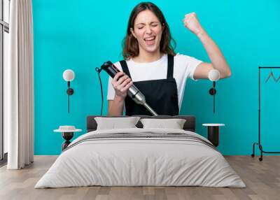 Young caucasian cooker woman using hand blender isolated on blue background celebrating a victory Wall mural