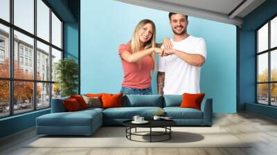 Young caucasian couple isolated on blue background bumping fists Wall mural