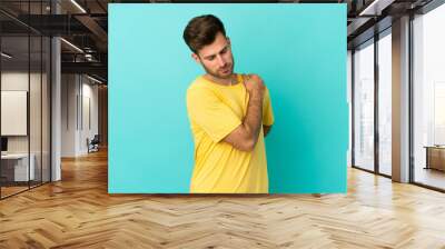 Young caucasian handsome man isolated on blue background suffering from pain in shoulder for having made an effort Wall mural