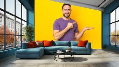 Young caucasian handsome man isolated on yellow background holding copyspace imaginary on the palm to insert an ad Wall mural