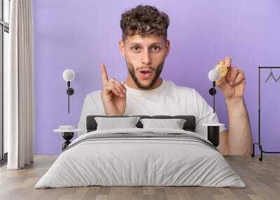 Young caucasian man holding a Bitcoin isolated on purple background intending to realizes the solution while lifting a finger up Wall mural