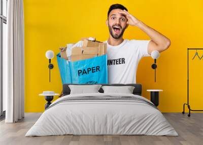 Young caucasian man holding a recycling bag full of paper to recycle isolated on white background with surprise expression Wall mural