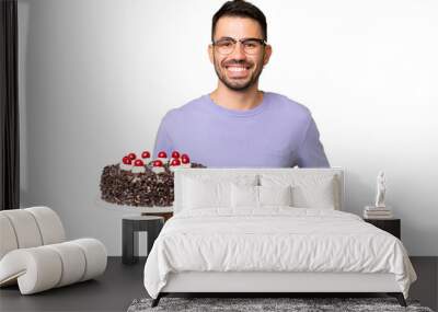 Young caucasian man holding birthday cake isolated on green chrome background posing with arms at hip and smiling Wall mural