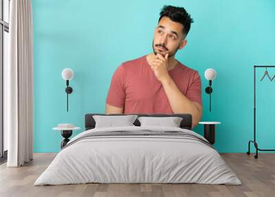 Young caucasian man isolated on blue background and looking up Wall mural