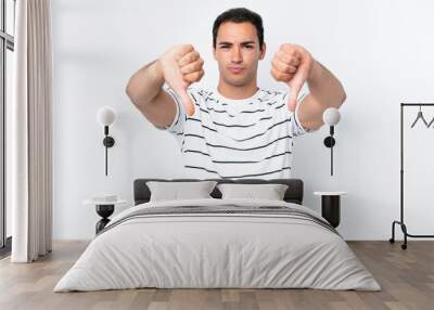 Young caucasian man isolated on white background showing thumb down with two hands Wall mural