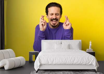 Young caucasian man isolated on yellow background with fingers crossing Wall mural