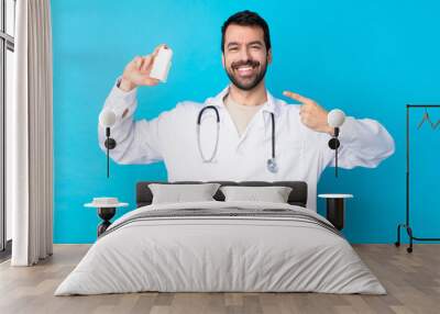 Young caucasian man over isolated background wearing a doctor gown and holding pills Wall mural