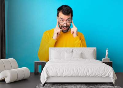 Young caucasian man over isolated blue background with glasses and surprised Wall mural