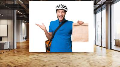 Young caucasian man taking a bag of takeaway food over isolated background with shocked facial expression Wall mural