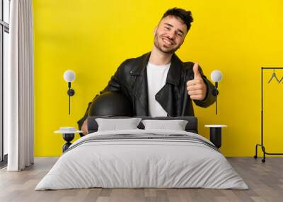 Young caucasian man with a motorcycle helmet isolated on yellow background with thumbs up because something good has happened Wall mural