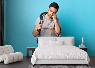 Young caucasian man with backpack and trekking poles isolated on blue background with tired and bored expression Wall mural