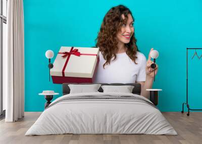 Young caucasian woman holding a gift isolated on blue background intending to realizes the solution while lifting a finger up Wall mural