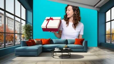 Young caucasian woman holding a gift isolated on blue background with happy expression Wall mural