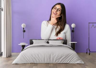 Young caucasian woman holding a piggybank isolated on purple background happy and smiling Wall mural