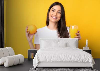 Young caucasian woman holding an orange over isolated yellow background Wall mural