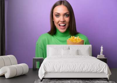 Young caucasian woman holding fried chips on purple background with surprise facial expression Wall mural