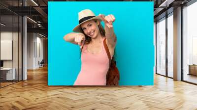 Young caucasian woman in summer holidays isolated on blue background points finger at you while smiling Wall mural