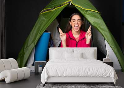 Young caucasian woman inside a camping green tent with fingers crossing Wall mural