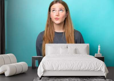 Young caucasian woman isolated on blue background and looking up Wall mural