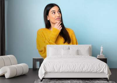 Young caucasian woman isolated on blue background having doubts Wall mural