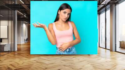 Young caucasian woman isolated on blue background having doubts Wall mural