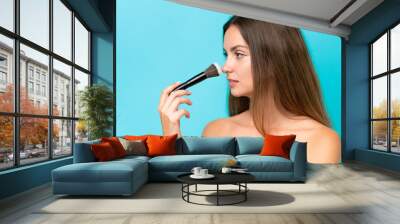 Young caucasian woman isolated on blue background holding makeup brush Wall mural