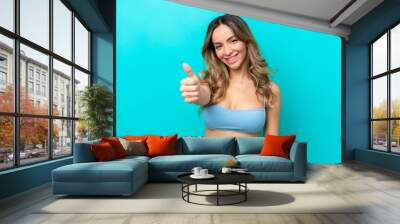 Young caucasian woman isolated on blue background in swimsuit in summer holidays and with thumb up Wall mural