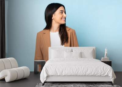 Young caucasian woman isolated on blue background looking to the side and smiling Wall mural