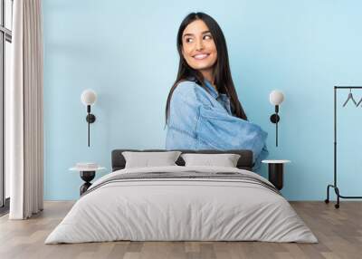 Young caucasian woman isolated on blue background looking to the side and smiling Wall mural