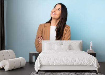 Young caucasian woman isolated on blue background looking up while smiling Wall mural